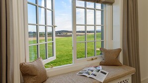 Ein Fensterplatz mit einem gemusterten Kissen, einer Zeitschrift und Blick auf ein grünes Feld.