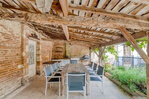 An outdoor dining area with a rustic wooden table and chairs, brick walls, and a pergola structure. - Maison Merisier - Six Bedroom Villa, Sleeps 14 (Montpon-Ménestérol)