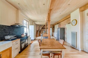 A spacious kitchen with a wooden table, a stove, and a brick wall. - Maison Merisier - Six Bedroom Villa, Sleeps 14 (Montpon-Ménestérol)