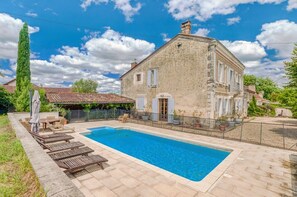 A rectangular swimming pool with a stone deck, a large stone building with a balcony, and a tall tree in the background. - Maison Merisier - Six Bedroom Villa, Sleeps 14 (Montpon-Ménestérol)