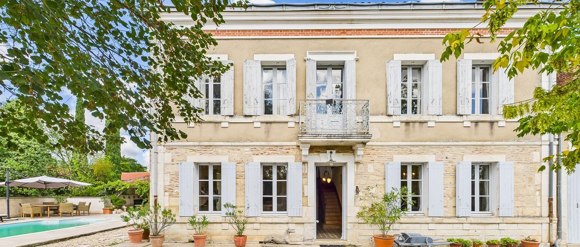 A two-story building with a swimming pool, outdoor seating, and potted plants.