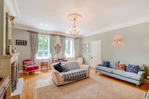 A living room with a fireplace, a sofa, a red armchair, a blue sofa, and a chandelier. - Maison Merisier - Six Bedroom Villa, Sleeps 14 (Montpon-Ménestérol)