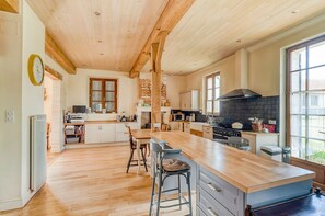 A spacious kitchen with wooden beams, a large island, and a view to the outside. - Maison Merisier - Six Bedroom Villa, Sleeps 14 (Montpon-Ménestérol)