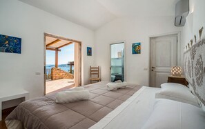 Ein Schlafzimmer mit Bett, Stuhl, Nachttisch und einer Tür, die auf einen Balkon mit Blick führt.