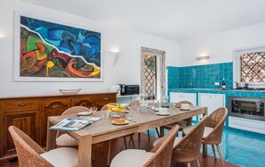 Ein Essbereich mit Holztisch, Korbstühlen und einem farbenfrohen abstrakten Gemälde an der Wand.