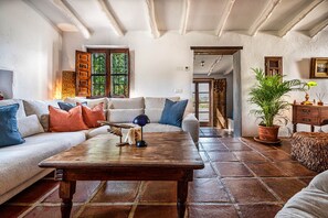 A cozy living room with a wooden coffee table, a sofa with colorful cushions, a potted plant, and a rustic wooden cabinet. - Cortijo Maria Camila (Alcaucín)
