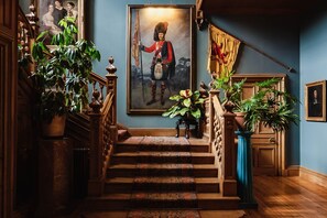 A grand staircase with ornate railings, a large framed portrait, and lush green plants.
