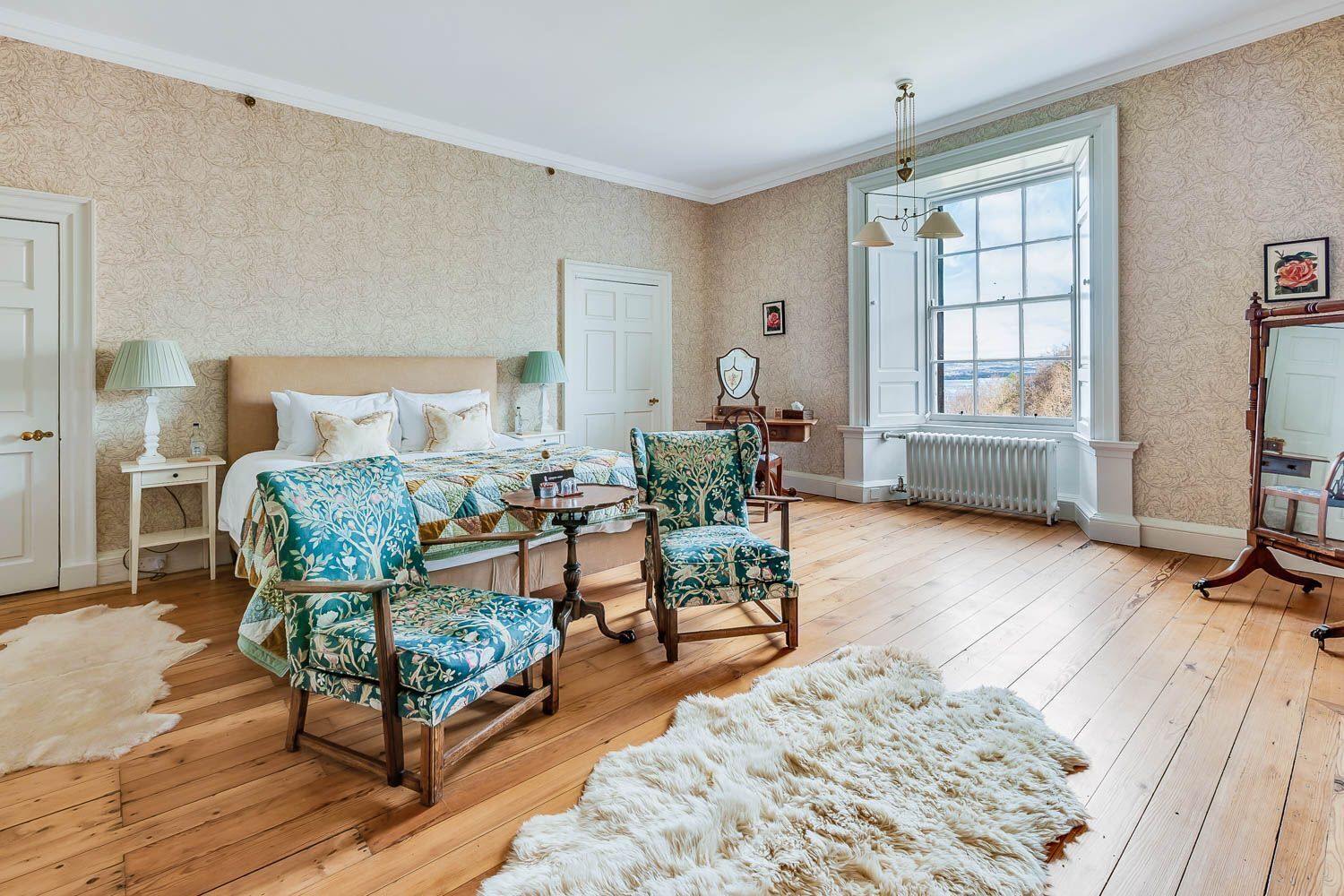 Une chambre à coucher avec un lit, deux chaises, une table, un radiateur et une fenêtre donnant sur un beau paysage.