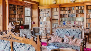 A library with bookshelves, a wooden sofa, and a fireplace.
