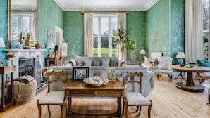 A room with a fireplace, a sofa, a dining table with chairs, and a large window.