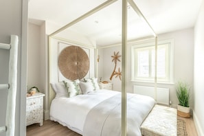 Ein Schlafzimmer mit Himmelbett, einer großen Wanddekoration und einem Fenster mit Jalousien.