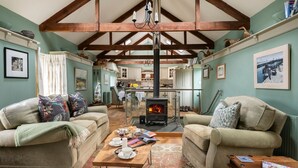 A cozy living room with a fireplace, two sofas, a coffee table, and a kitchen in the background.