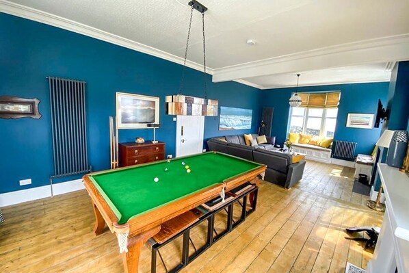A pool table in a room with blue walls, a sofa, and a window.