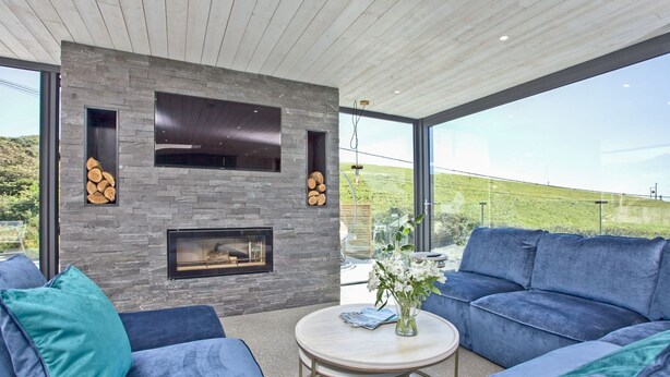 Una sala de estar moderna con chimenea de piedra, ventanas amplias y un sofá azul.