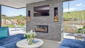 Un espacio exterior moderno con chimenea de piedra, asientos y vistas del paisaje.
