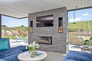 A modern outdoor living area with a stone fireplace, seating, and a view of the landscape.