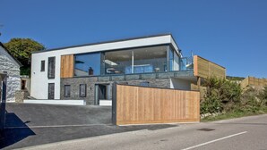 Una casa moderna de dos pisos con ventanas amplias, un balcón y una valla de madera.