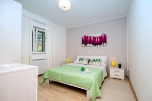 Ein Schlafzimmer mit Bett, Nachttisch, Gardinen, Heizkörper und einem Bild an der Wand.