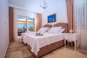 Ein Schlafzimmer mit Bett, Nachttischen, einer Chandelüster und Blick durch ein Fenster.