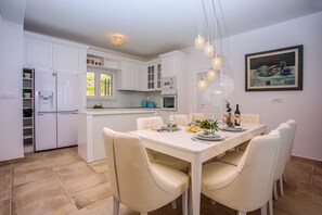 A modern kitchen with white cabinets, a dining table with chairs, and pendant lights. - Villa Bufo - Four Bedroom Villa, Sleeps 10 (Mimice)