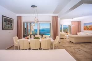 Ein Essbereich mit Tisch und Stühlen, einer Kronleuchter und Blick auf das Meer.
