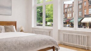 Una camera da letto con un letto grande, un termosifone, una finestra vista edifici e una lampada a sospensione.