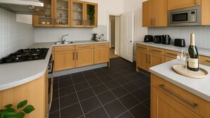 Una cucina moderna con mobili in legno, piano cottura a gas, forno a microonde e una bottiglia di vino su un vassoio.