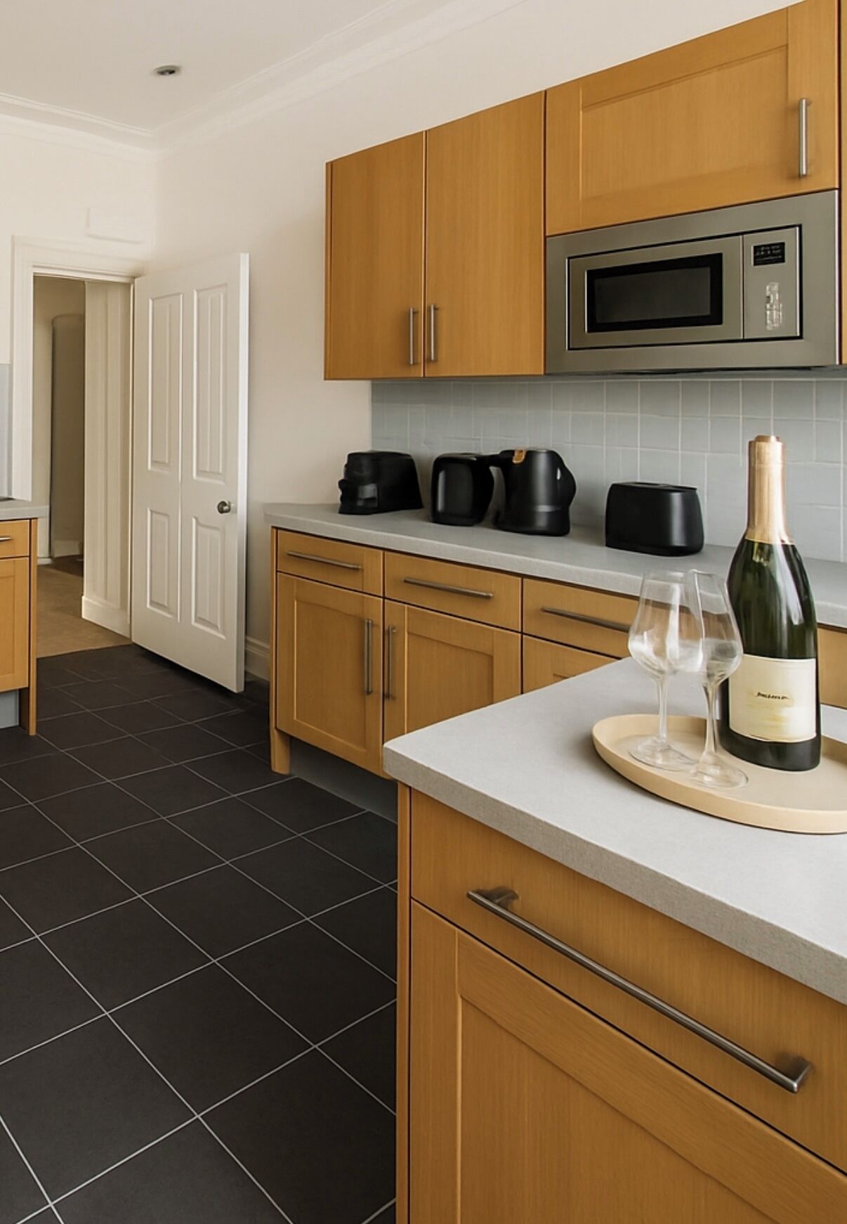 A modern kitchen with wooden cabinets, a stainless steel microwave, and a wine bottle on the counter.