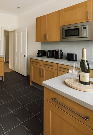 A modern kitchen with wooden cabinets, a stainless steel microwave, and a wine bottle on the counter. - J-Pantheon of Covent G - 2Bed 2 Bath with AC (London)