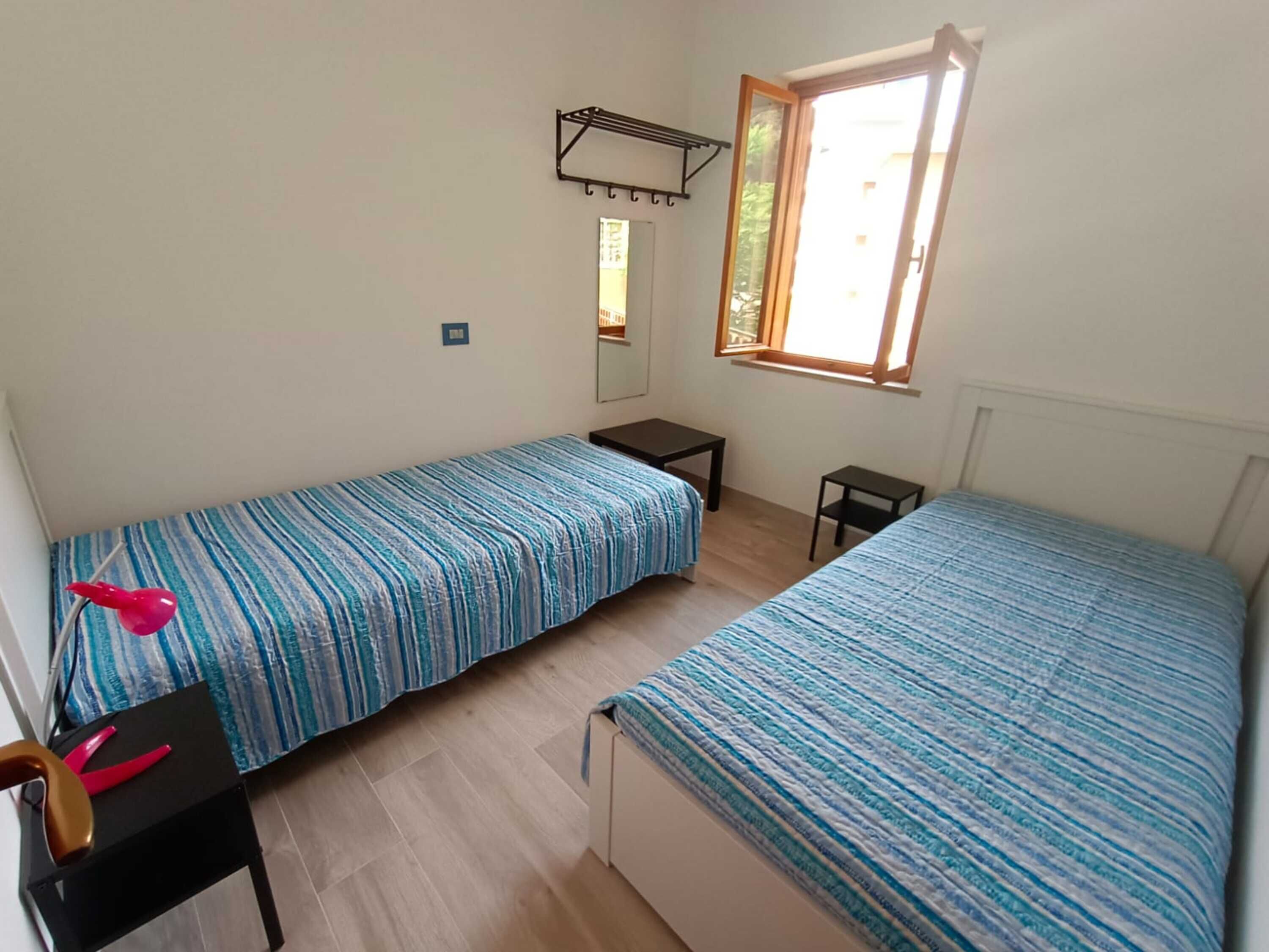 Une chambre avec deux lits, une petite table, une chaise, un miroir et une fenêtre.