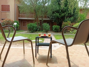 Een binnenplaats met twee metalen stoelen, een kleine tafel met eten en drinken, en een gebouw met een balkon op de achtergrond.