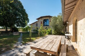 A rustic outdoor area with a wooden table and benches, a stone pathway, and a building with a tiled roof and window. - Chateau Art De Vivre (Saint-Christoly-Médoc)