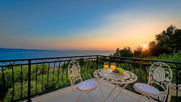 Ein Balkon mit Tisch und Stühlen, mit Blick auf ein Gewässer und viel Grün.