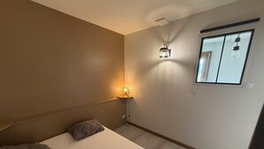 A bedroom with a bed, a bedside lamp, a window, and a wall-mounted light fixture. - Urban cocoon with panoramic view - Balcony - Fully equipped (Saint-Étienne)