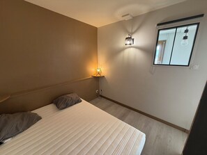 Ein Schlafzimmer mit Bett, Nachttischlampe, Fenster und einer Wandleuchte.