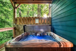 Ein Whirlpool mit einer Holzterrasse und Holzzaun, umgeben von Bäumen.