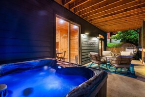 Un jacuzzi, terraza de madera, sillas de mimbre y un porche cubierto.