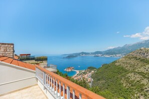 Blick auf die Küste vom Balkon aus, mit einer Steinmauer, klarem, blauem Meer und einer kurvenreichen Straße, die zu einem Dorf führt.