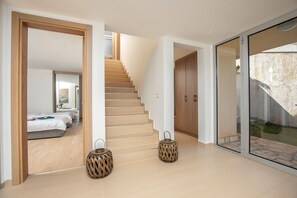 Ein modernes Hotelinnere mit einer Treppe, die zu einem Schlafzimmer führt, einer Glastür zu einem Außenbereich und zwei dekorativen Holzschemeln.