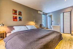 Ein modernes Schlafzimmer mit einem großen Bett, einem Sessel, einem Schreibtisch und einem Fenster.