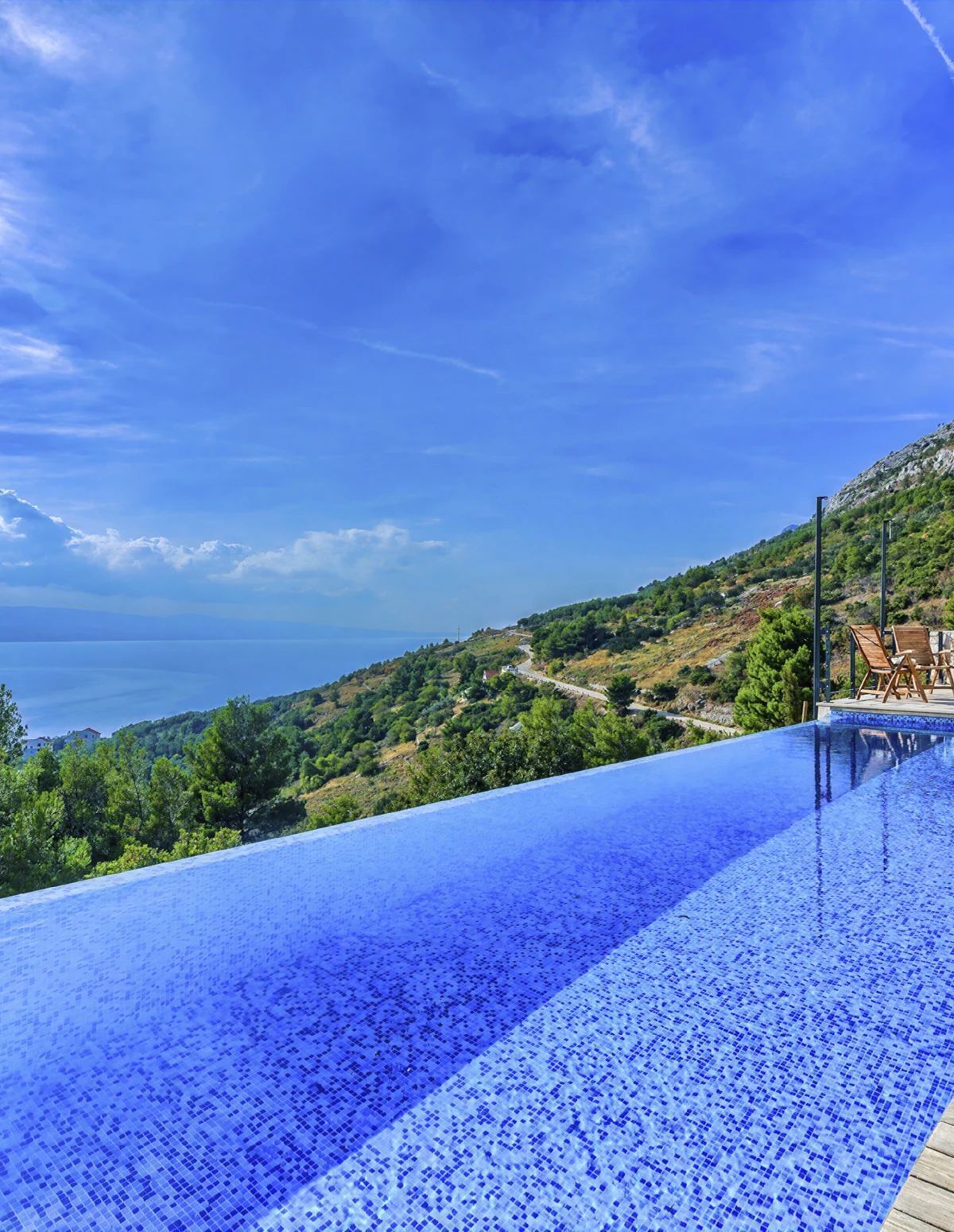 Ein Pool ohne Ende mit freiem Blick auf das Meer und eine Hügelkette.