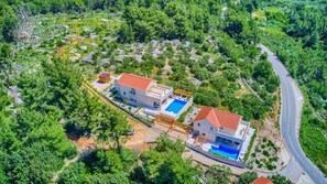 Ein zweistöckiges Haus mit Swimmingpool, umgeben von üppiger Vegetation und einer gewundenen Straße.