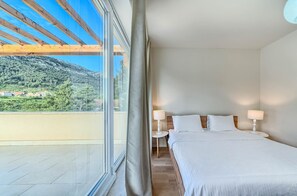 Ein Hotelzimmer mit einem Bett, zwei Nachttischlampen, einem Fenster mit Vorhängen und Blick auf eine gebirgige Landschaft.