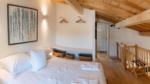 Ein Schlafzimmer mit Bett, Kissen, einem Wandbild, Holzboden und einem Gang zu einer Tür.