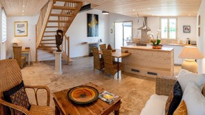 Ein geräumiger Wohnbereich mit einer Holztreppe, einem Esstisch, Korbmöbeln und einer Küche mit einer Holz Arbeitsplatte.