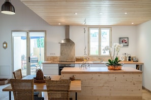 Eine moderne Küche mit Holzboden, einer zentralen Kochinsel und einem Essbereich mit Korbmöbeln.