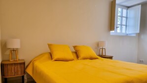 Uma cama com colcha amarela, duas mesas de cabeceira com abajures e uma janela com vista para o verde.
