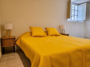 Ein Bett mit gelber Bettdecke, zwei Nachttische mit Lampen und ein Fenster mit Blick auf Grünflächen.