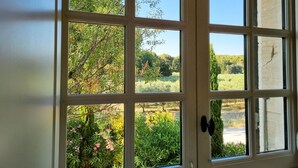 Uma janela com vários painéis, uma porta com maçaneta e vista para vegetação e árvores lá fora.