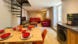 Uma sala de jantar com mesa de madeira posta para quatro pessoas, um sofá vermelho e uma escada em espiral.